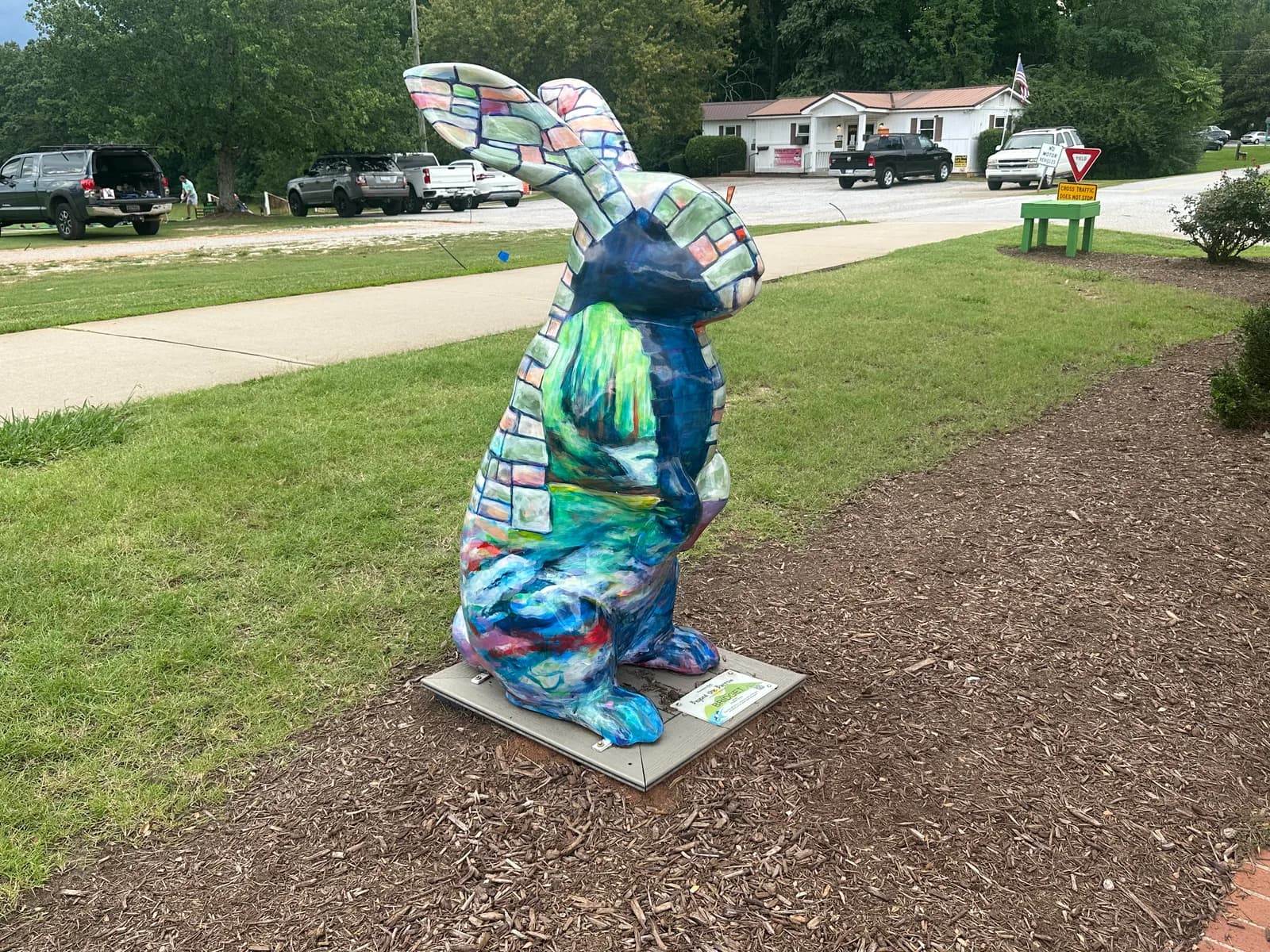 One of the hand painted rabbit sculptures from the Beyond the Burrow public art project, standing on a mulched bed near a street in Travelers Rest, South Carolina