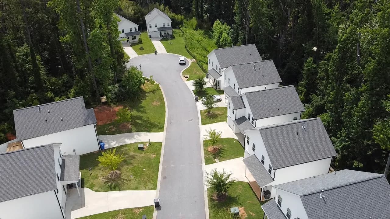 Aerial view of new single family rental homes along a curved street backed by woods at Village West in Travelers Rest, South Carolina